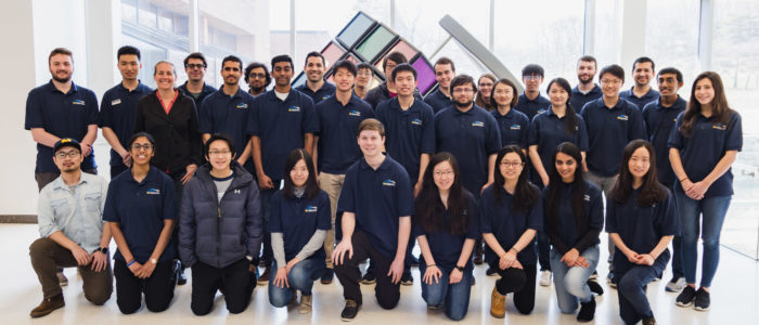 A large team posing in front of the North Campus Rubik's cube